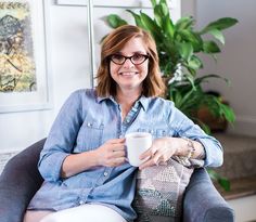 a woman sitting in a chair holding a coffee cup and smiling at the camera while wearing glasses