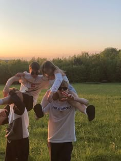 a group of people standing on top of each other in a field with the sun setting behind them