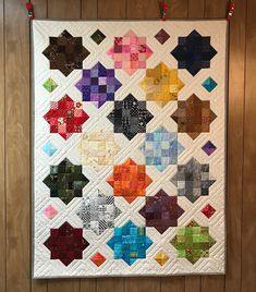 a colorful quilt hanging on the wall next to a wood paneled wall with red string lights