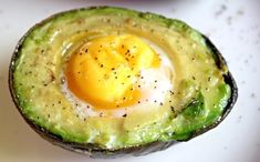 an avocado with an egg in it on a white counter top next to some other food