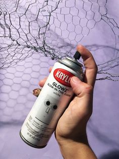 a person holding a can of kryll glue in front of a chicken wire net