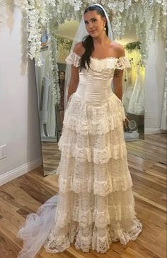 a woman standing in front of a mirror wearing a wedding dress with ruffled layers