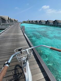 a bicycle is parked on a pier near the ocean and over water huts are in the background