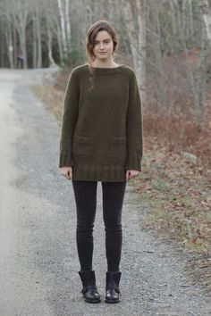 a woman standing in the middle of a road wearing black boots and a green sweater