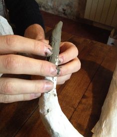 a person holding a knife in their hand over a piece of pottery on a wooden table