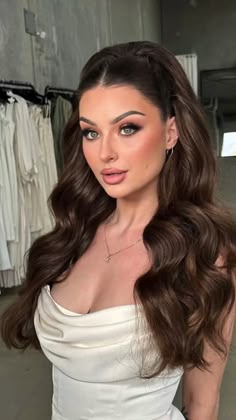 a woman with long brown hair wearing a white dress and posing in front of clothes