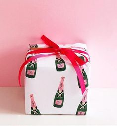 a wrapped gift box with pink ribbon and wine bottles on it, against a pink background