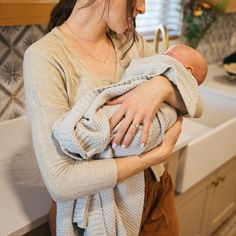 a woman holding a baby in her arms while standing next to a sink and counter