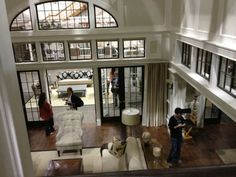 two people standing in the middle of a large living room with high ceilings and lots of windows