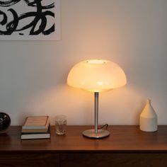 a table lamp sitting on top of a wooden desk next to a vase and book