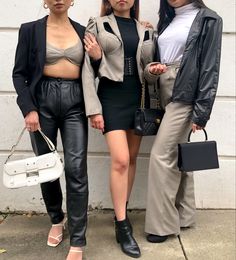 three women standing next to each other in front of a white wall wearing black leather pants