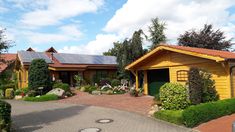 a yellow house with solar panels on the roof and landscaping around it's perimeter