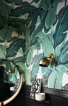 a bathroom with green leaves on the wall and black counter top, gold faucet