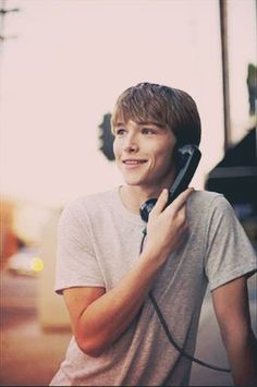 a young man talking on a cell phone while standing next to a pole with a street light in the background