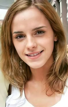 a close up of a person wearing a white shirt and smiling at the camera with long hair