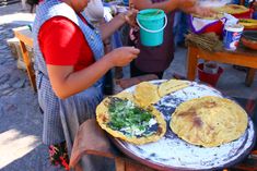 a woman is making tortillas on an outdoor grill with other people around her