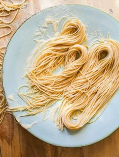 some noodles are on a blue plate next to a knife and fork, which is sitting on a wooden table