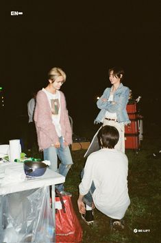 two women and a man are standing near a table with food on it at night