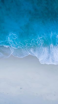 an aerial view of the ocean with waves crashing in to shore and people walking on the beach