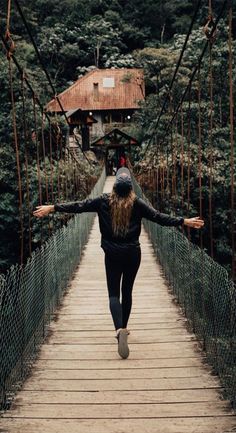 a woman walking across a suspension bridge in the woods with her arms spread wide open