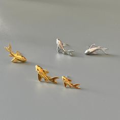 four different types of gold and silver fish studs on a gray surface with white background