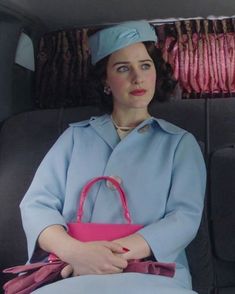 a woman sitting in the back seat of a car holding a pink purse and looking off into the distance