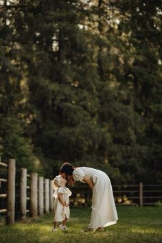 a woman in white dress holding a small child's head while standing next to a fence