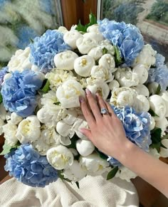 a woman's hand on top of a bouquet of blue and white flowers