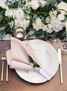 a place setting with white flowers and greenery