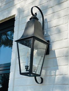 an old fashioned light hanging on the side of a white brick building next to a window