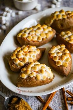 baked sweet potatoes with marshmallow toppings on a white plate next to cinnamon sticks