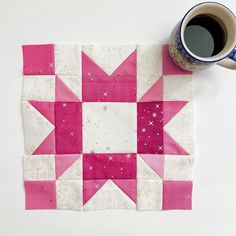 a cup of coffee sitting on top of a table next to a pink and white quilt