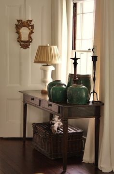 a table with two vases on it in front of a window and a lamp