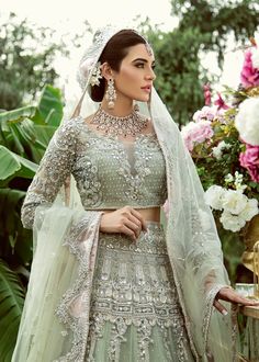 a woman wearing a green lehenga and matching jewelry with flowers in the background