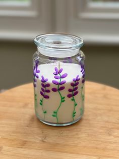 a glass jar filled with purple flowers sitting on top of a wooden table next to a window