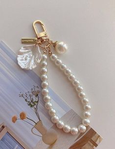 a white pearl necklace on a gold plated keychain next to a vase with flowers