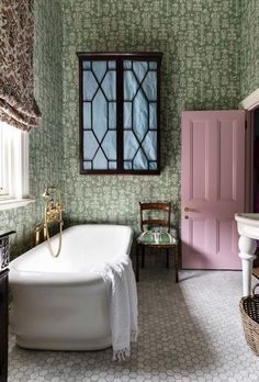 a bath tub sitting next to a pink door in a green and white tiled bathroom