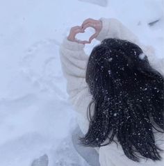 a woman standing in the snow making a heart shape with her hands