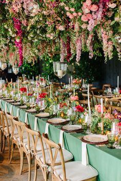 a long table with many flowers hanging from it's ceiling and place settings on the tables