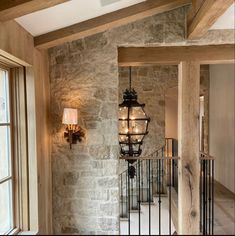 a light hanging from the side of a stone wall next to a stair case in a home