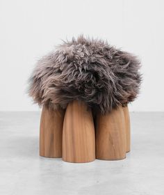 a pair of wooden stools with fur on them sitting on concrete floor next to white wall