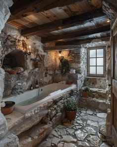 a bathroom with stone walls and flooring has a large tub in the corner, surrounded by potted plants