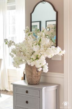 a vase filled with white flowers sitting on top of a dresser next to a mirror