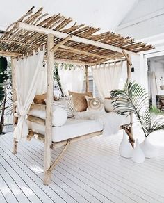 a canopy bed with white curtains and pillows on the floor next to potted plants