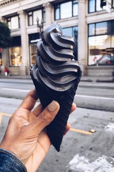 a hand holding up a black object in front of a building on a street corner