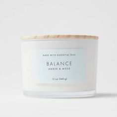 a white candle with a wooden lid and label that says balance amber & moss on it