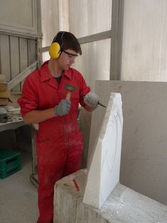 a man in red overalls and headphones working on a piece of white marble