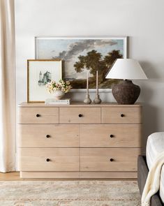 a bedroom scene with focus on the chest of drawers and artwork hanging above it's head