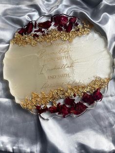 a white plate with gold and red flowers on it's side, surrounded by satin material