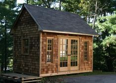 a small wooden cabin in the woods with windows on it's sides and doors open